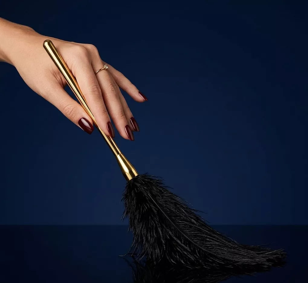 Hand holding a black ostrich feather teaser against a dark blue background