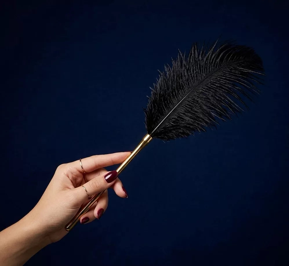 Hand holding a black feather teaser from real ostrich feather and a removable gold handle 
